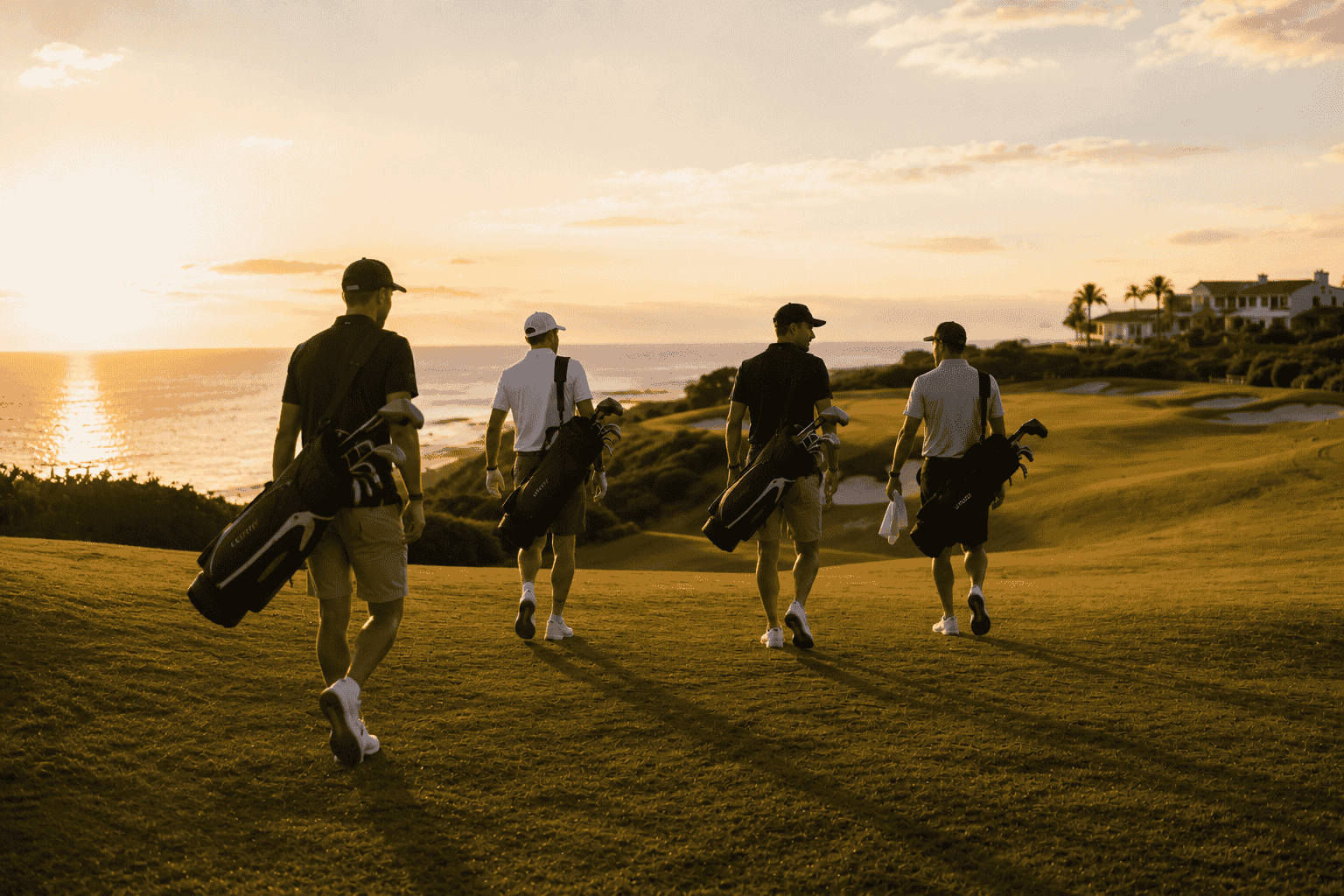 Two golfers walking a fairway with their bags at sunset